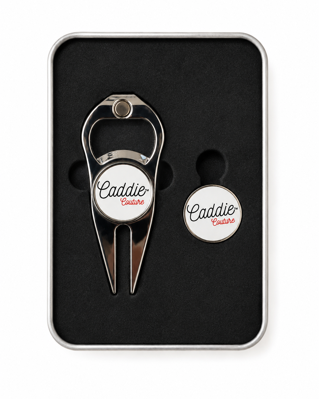A silver metal golf divot tool and matching circular tag set, both featuring a white circular center with the script logo 'Caddie Centre', presented in a black foam-lined gift box with a silver metal border.