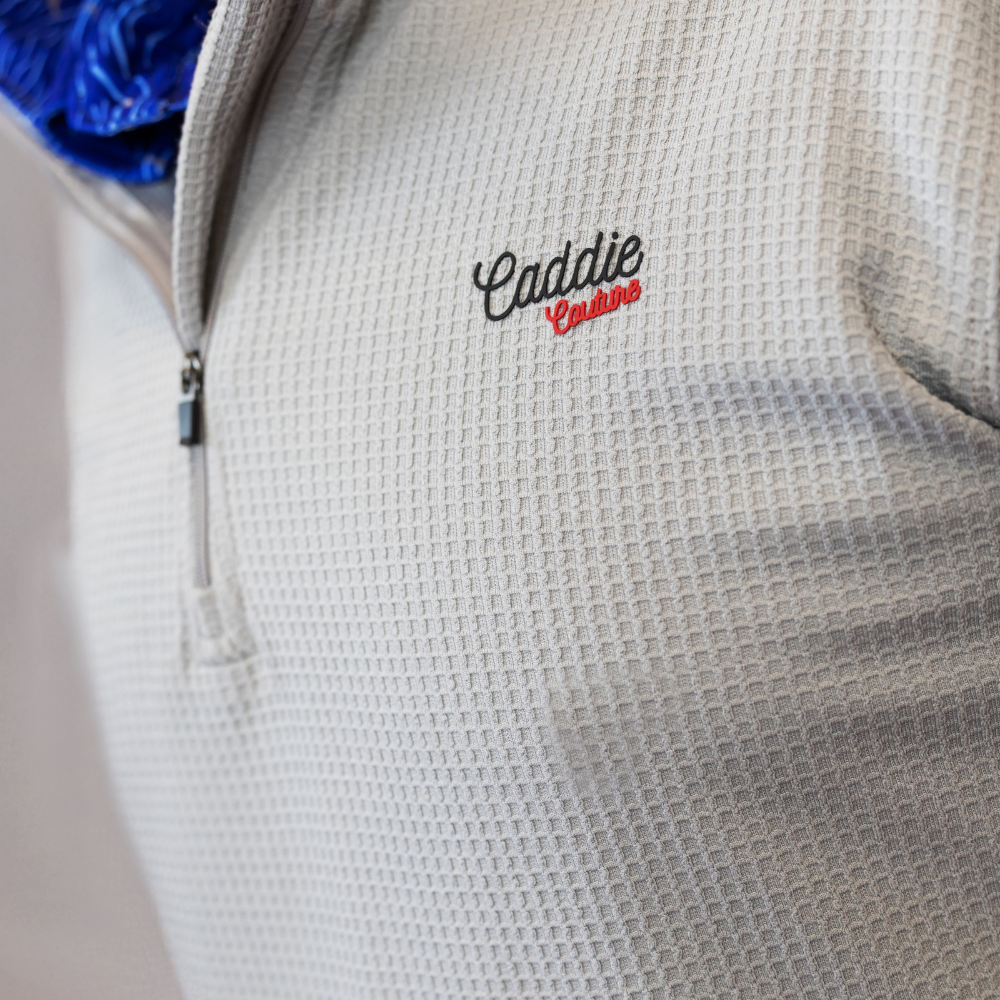 Close-up of a textured gray jacket with 'Caddie' embroidery on a neutral background