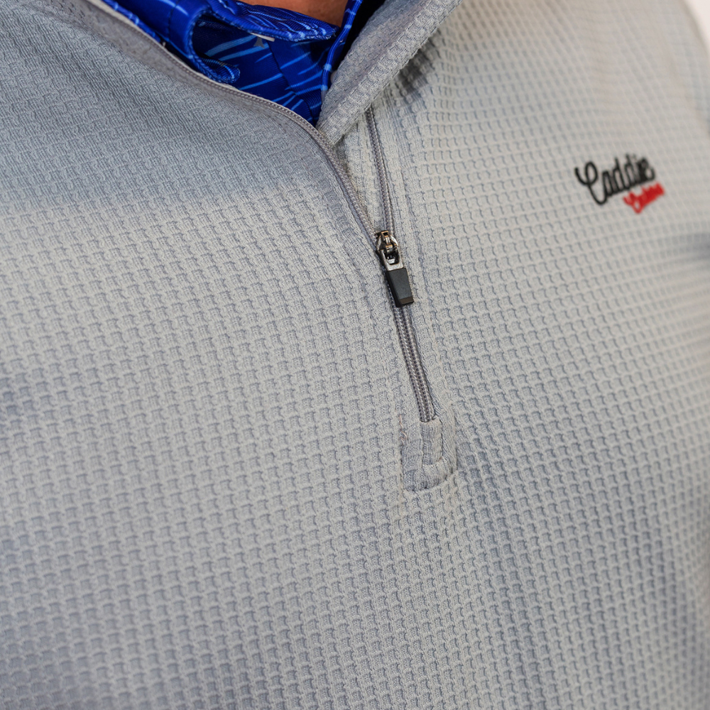 Close-up of a gray textured pullover with a zipper and 'Caddie' logo on a blue background.