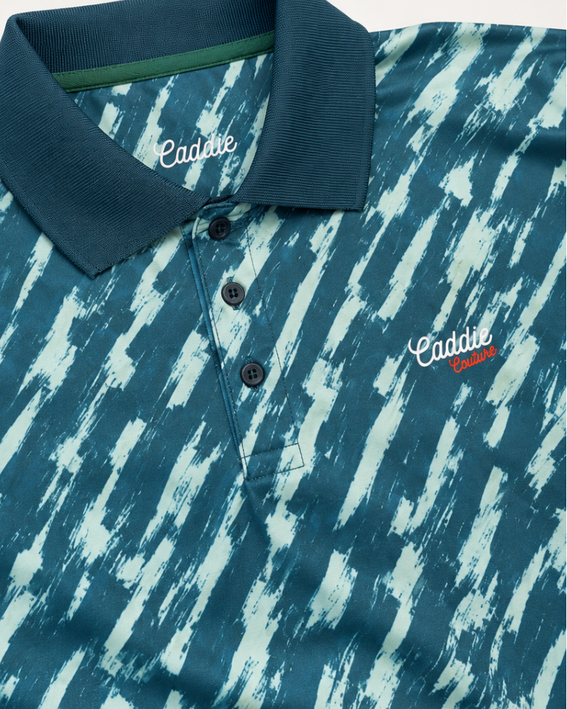 Close-up of a Caddy polo shirt featuring a blue and white abstract brushstroke pattern, with a solid dark blue collar and white embroidered logo.