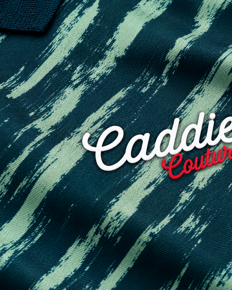 Close-up of a dark teal fabric with a light mint abstract brushstroke pattern and an embroidered 'Caddie Couture' logo in white and red.