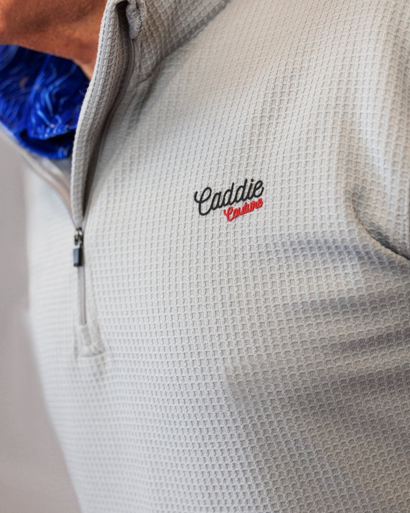 Close-up of a textured gray jacket with 'Caddie Couture' embroidery on a neutral background