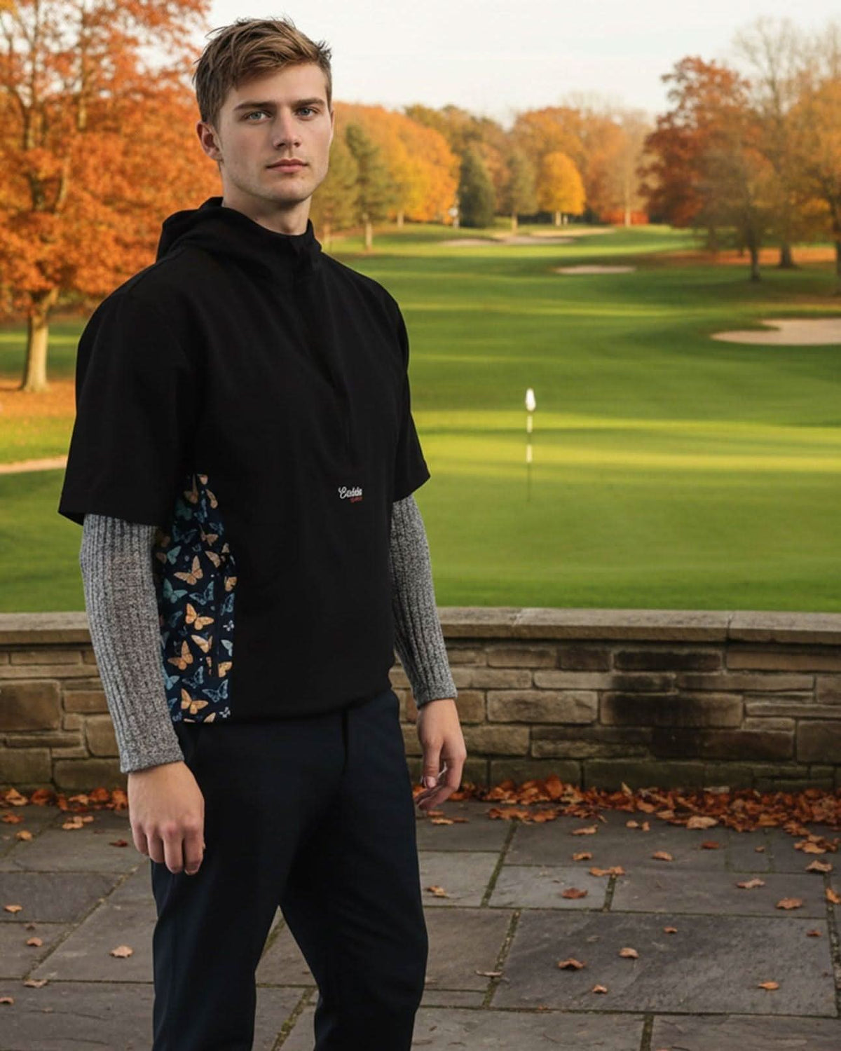 Man standing on a golf course wearing a black windbreaker jacket with a brand logo.