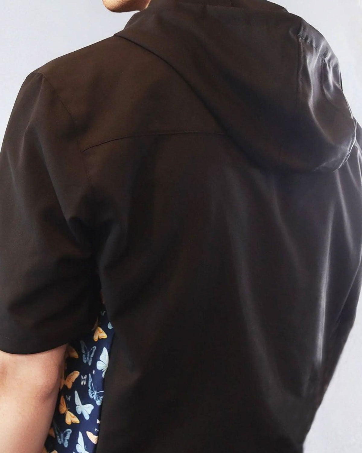 Person wearing a black windbreaker jacket with a butterfly patterned sides on a white background