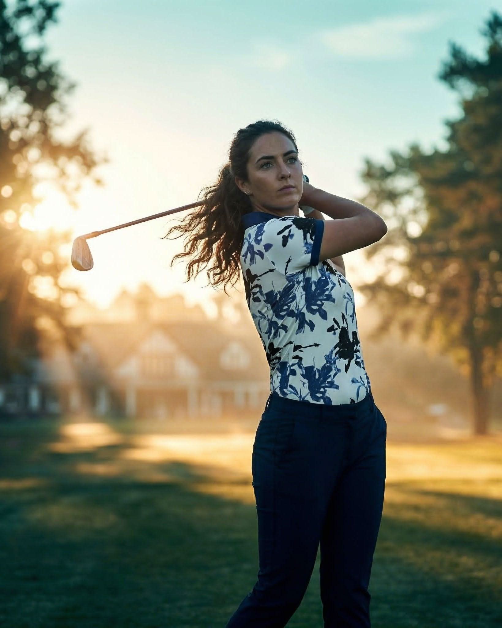 Woman holding a golf club on a golf course with trees and sunset in the background