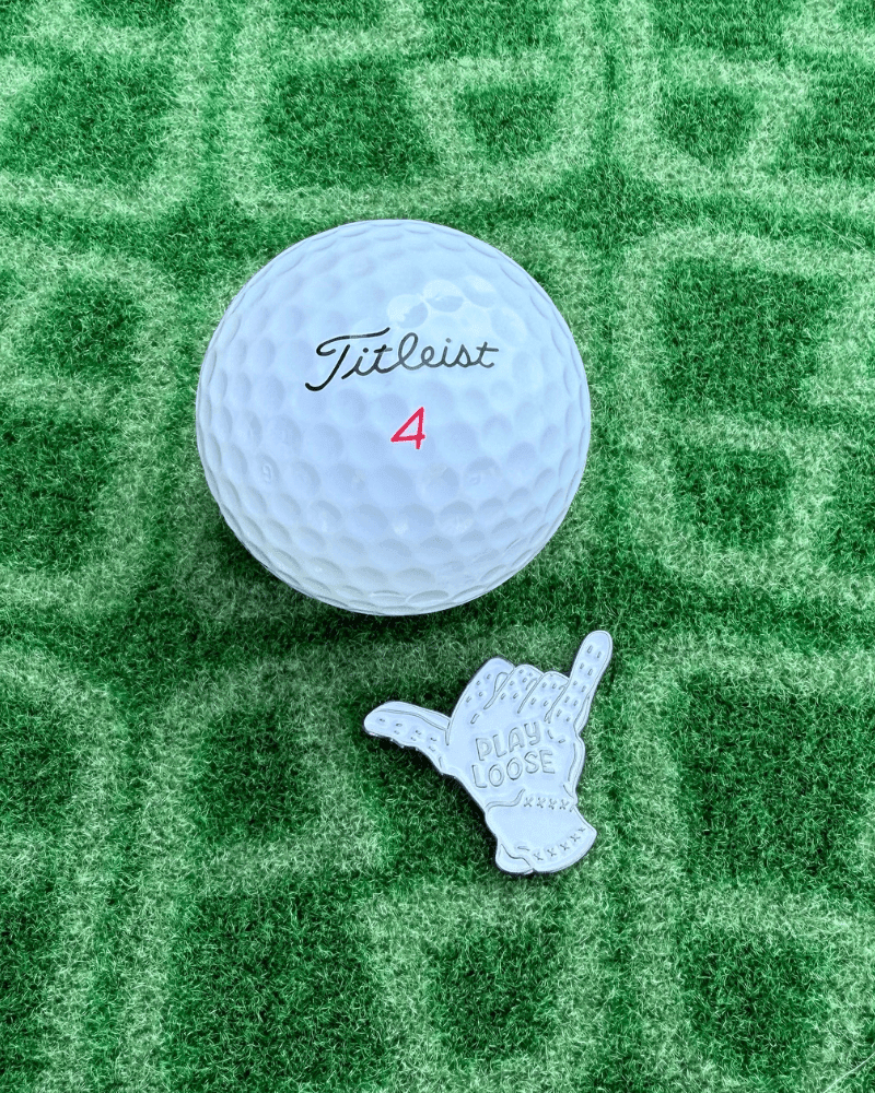 Titleist golf ball with a glove shaped golf ball marker on a green textured surface