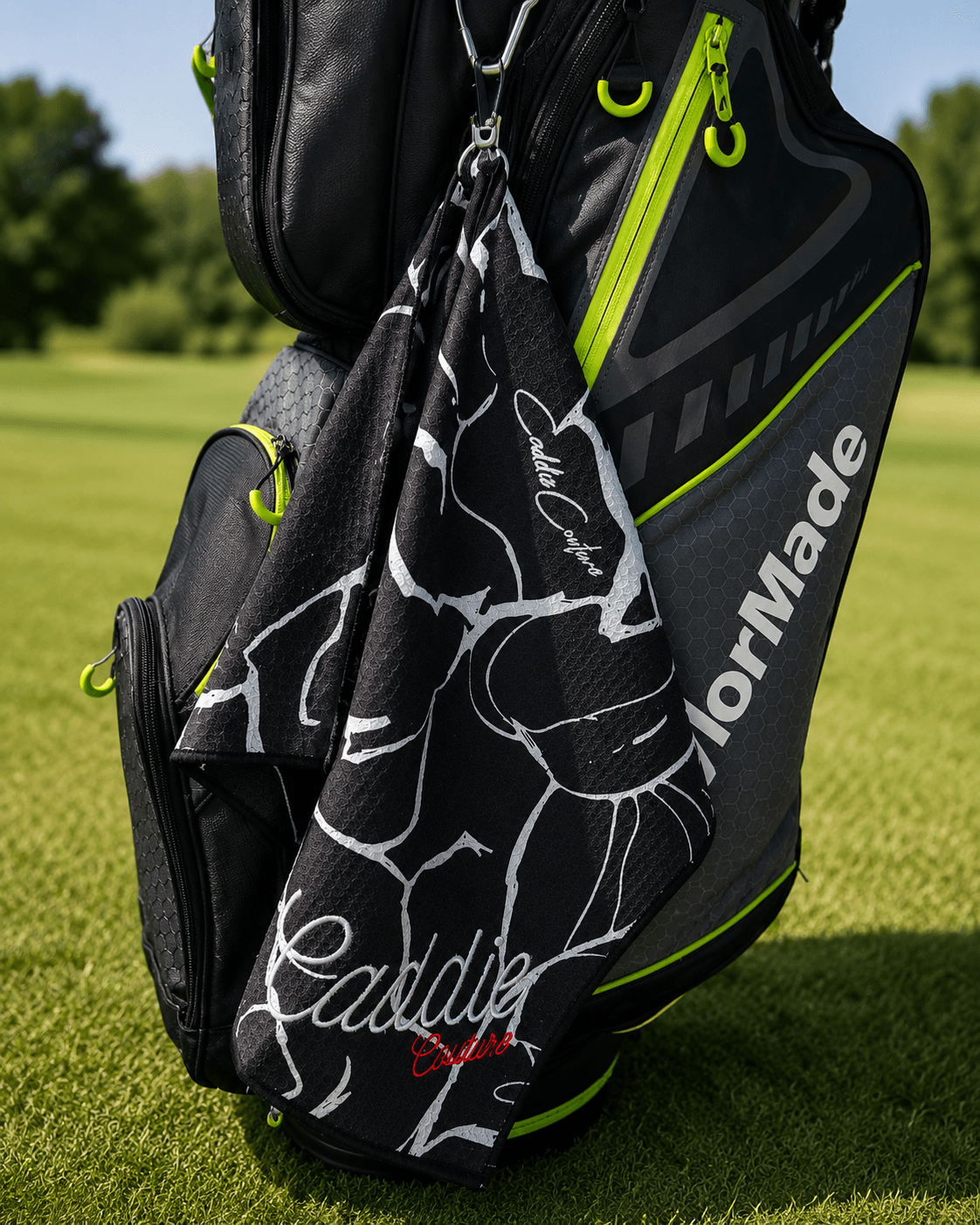 Golf bag with a black and white golf towel featuring 'Caddie' branding on a grassy background.