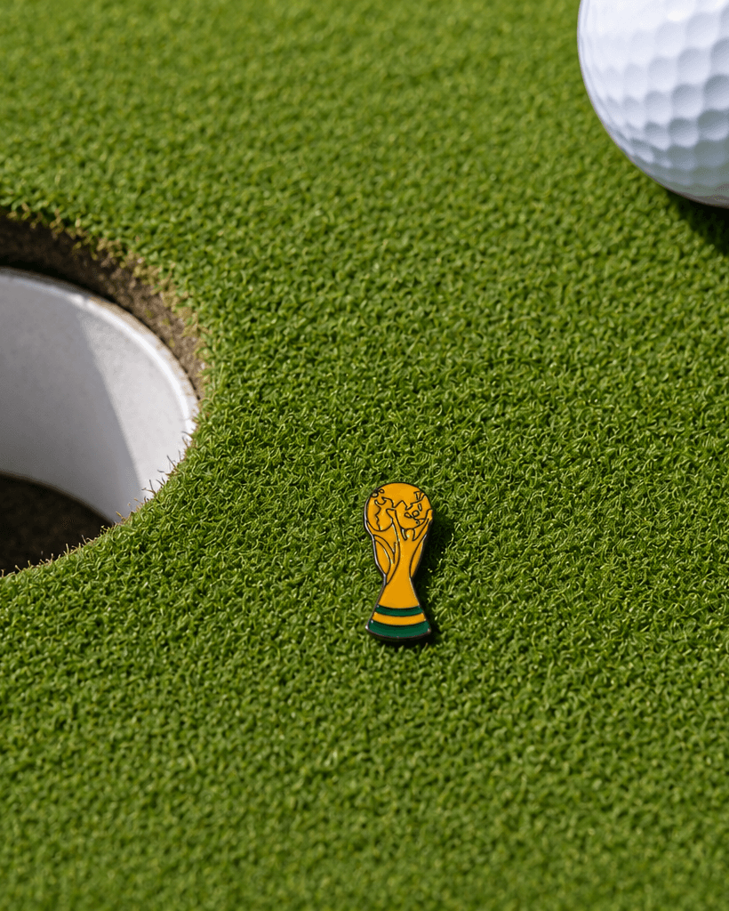 Golf ball near a hole with a miniature World Cup trophy on a green surface