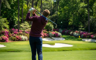 man hitting golf ball on course - spring weather wearing golf hoodie