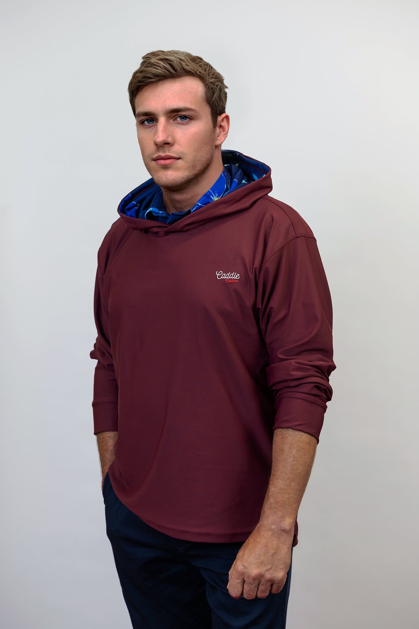 Man wearing a maroon golf hoodie with a logo on a white background
