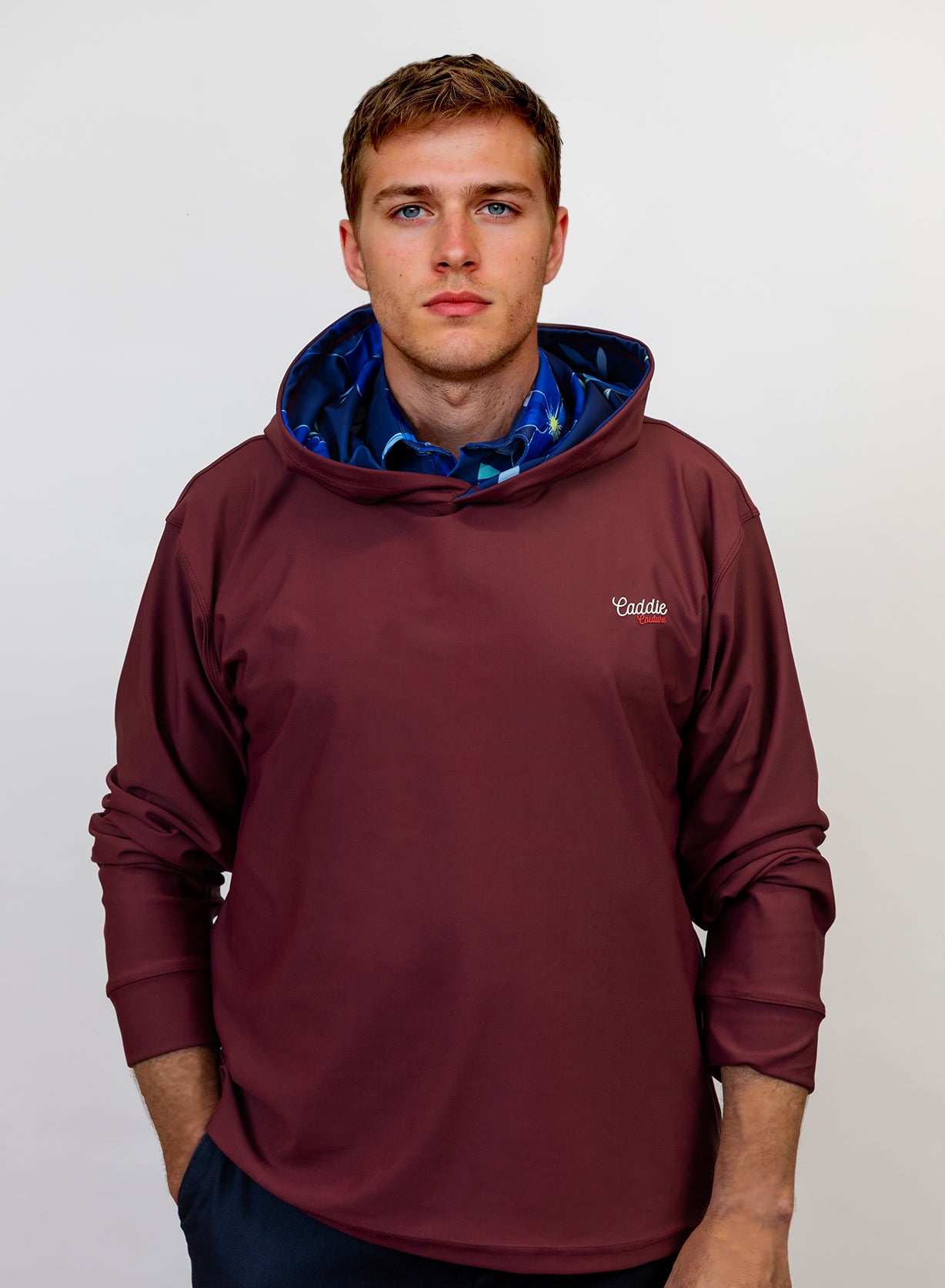 Man wearing a maroon golf hoodie with a blue lining on a plain background