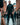 Man in a dark outfit walking down a busy street with brick buildings.