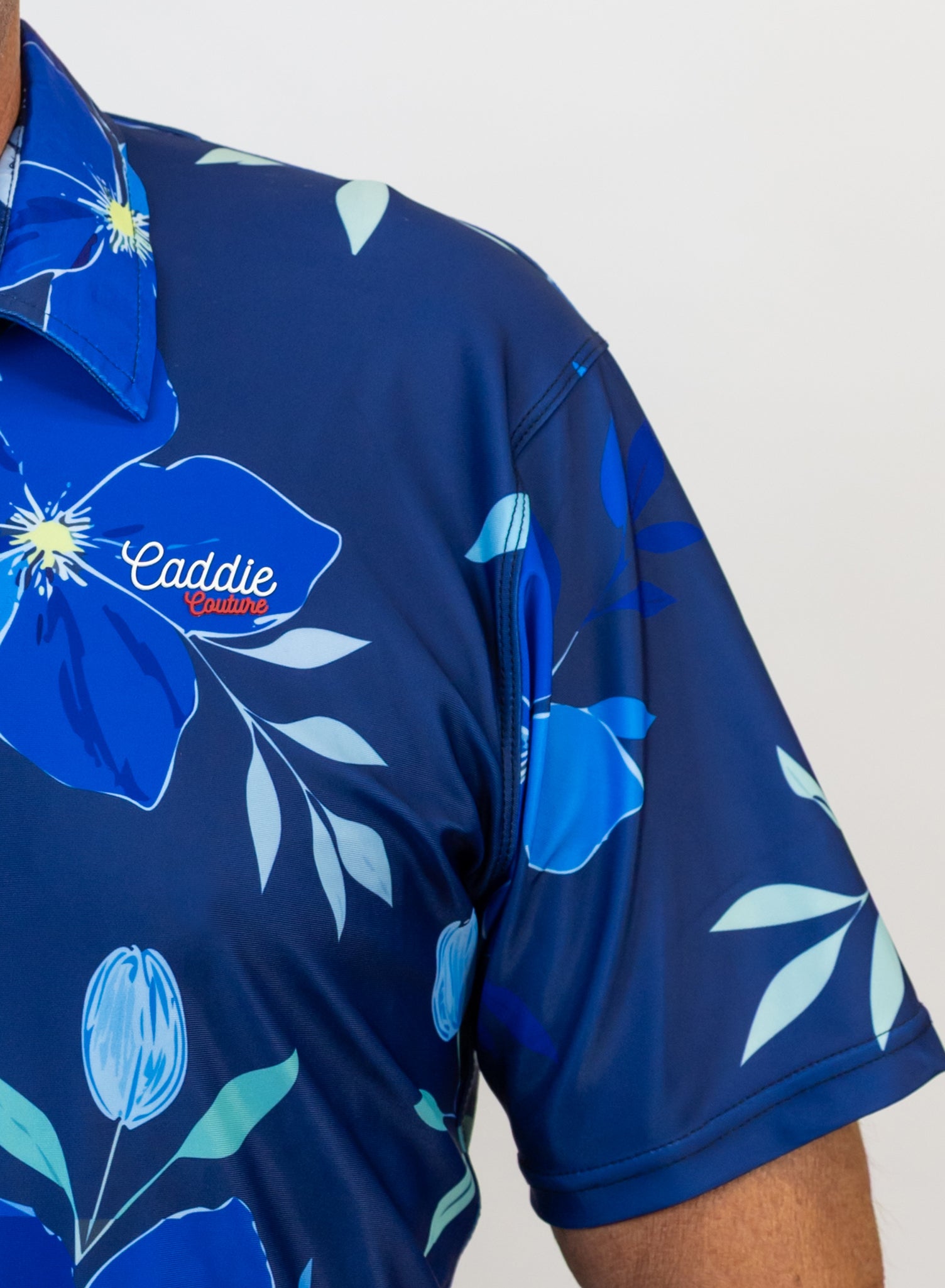 Navy blue golf shirt with floral design and 'Caddie Couture' branding on a white background
