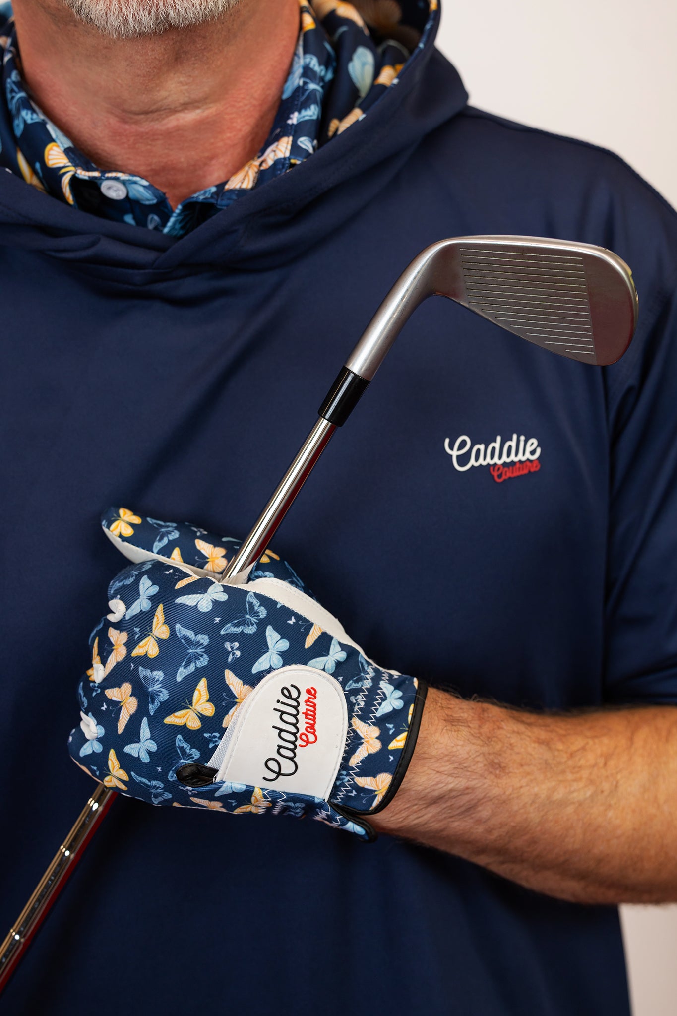 Person wearing a navy blue hoodie with 'Caddie' logo, holding a golf club and glove.