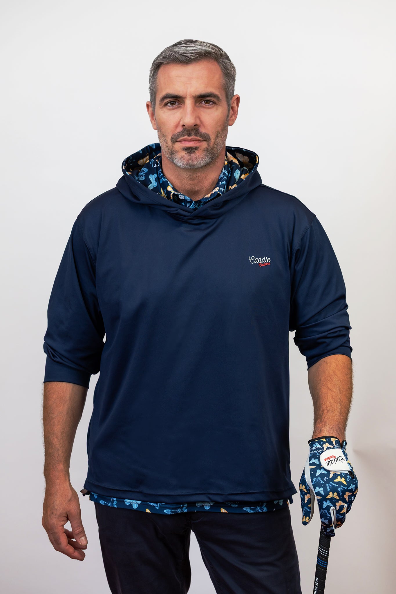 Man wearing a navy blue hoodie with a brand logo, holding a golf club and glove.
