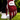 A close-up of a person's hand wearing a red and black patterned Caddie golf glove, holding a golf ball on a tee over a grassy golf course.