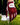 A close-up of a person's hand wearing a red and black patterned Caddie golf glove, holding a golf ball on a tee over a grassy golf course.