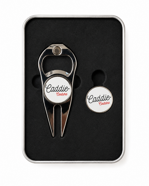 A silver metal golf divot tool and matching circular tag set, both featuring a white circular center with the script logo 'Caddie Centre', presented in a black foam-lined gift box with a silver metal border.