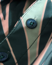 Close-up of a striped garment fabric with dark green, black, and light pink vertical stripes, featuring a dark blue button with 'COUTURE CADIE' embroidered on it.