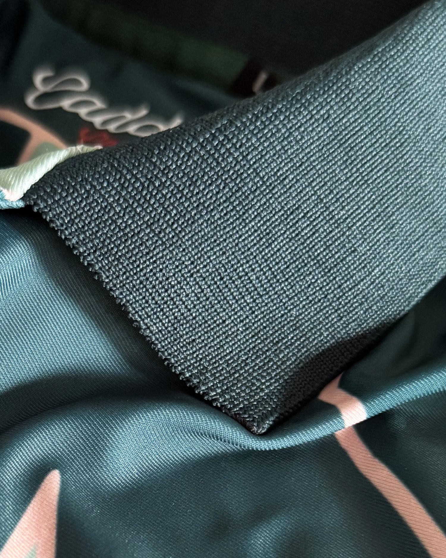 Close-up of a dark teal-green textured knit collar layered over a satin-like garment with pink and white abstract line patterns.