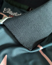Close-up of a dark teal-green textured knit collar layered over a satin-like garment with pink and white abstract line patterns.
