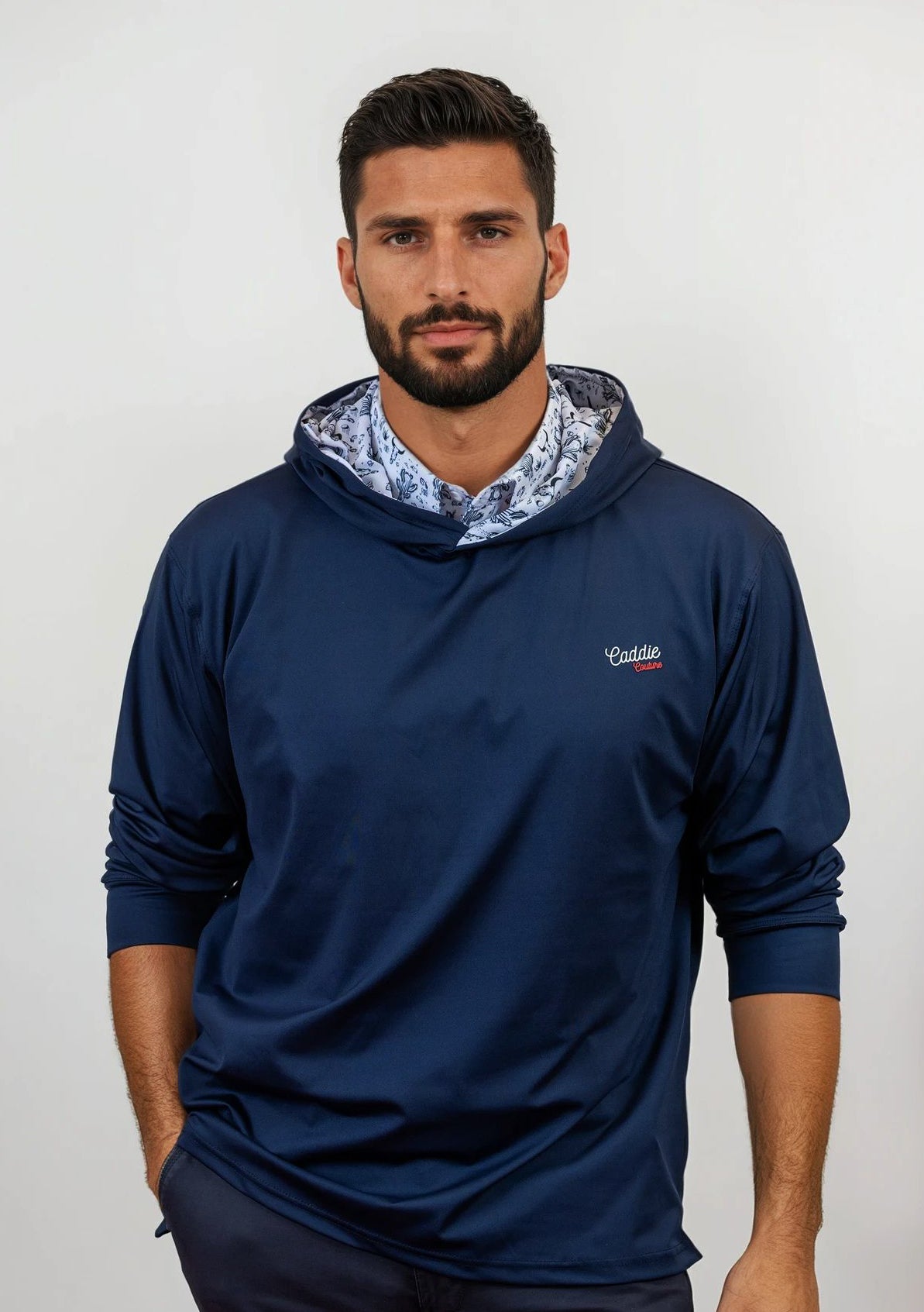 Man wearing a navy blue golf hoodie with a patterned lining on a white background