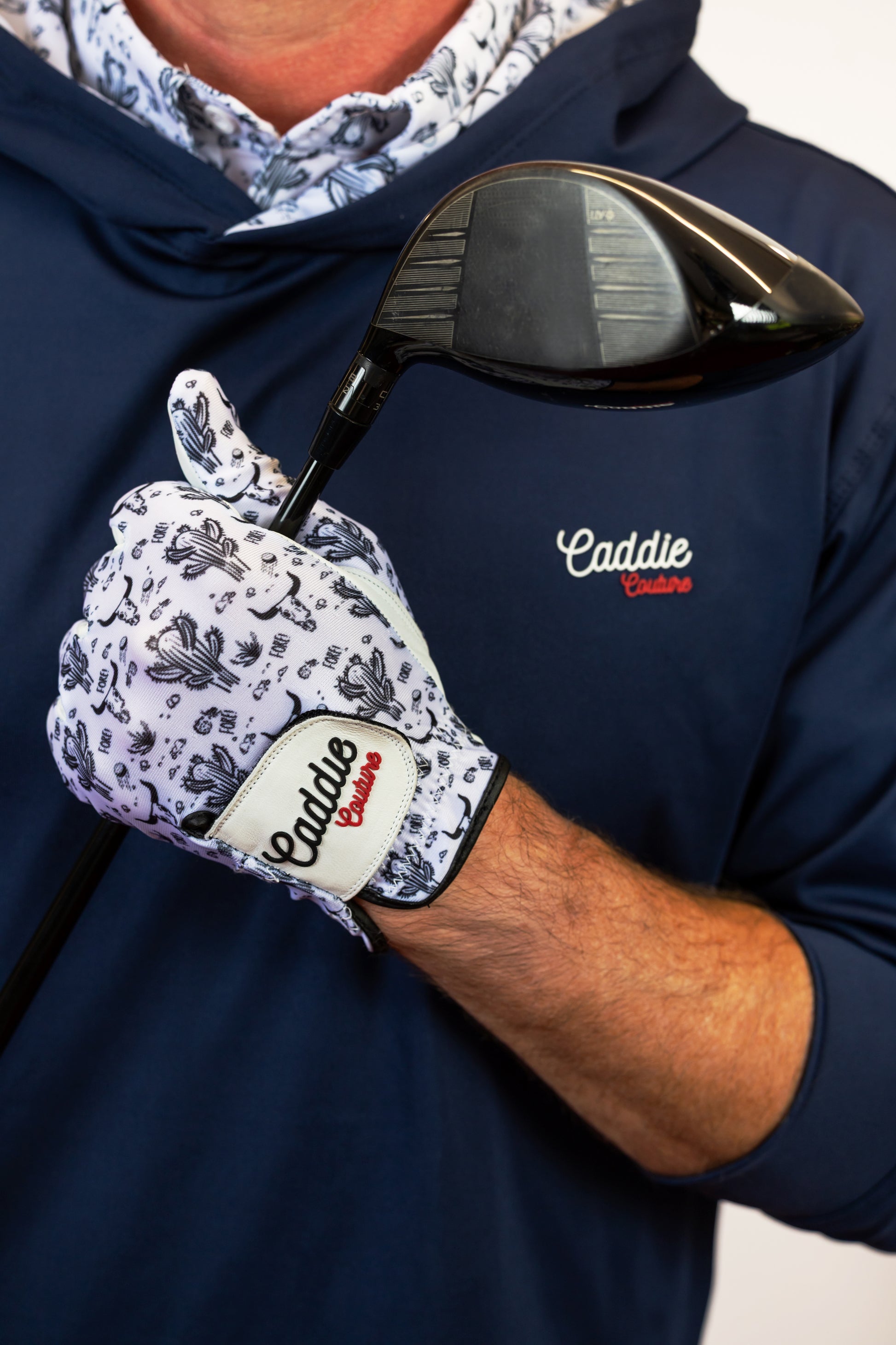 Person wearing a navy hoodie with 'Caddie' branding, holding a golf club with a matching glove.