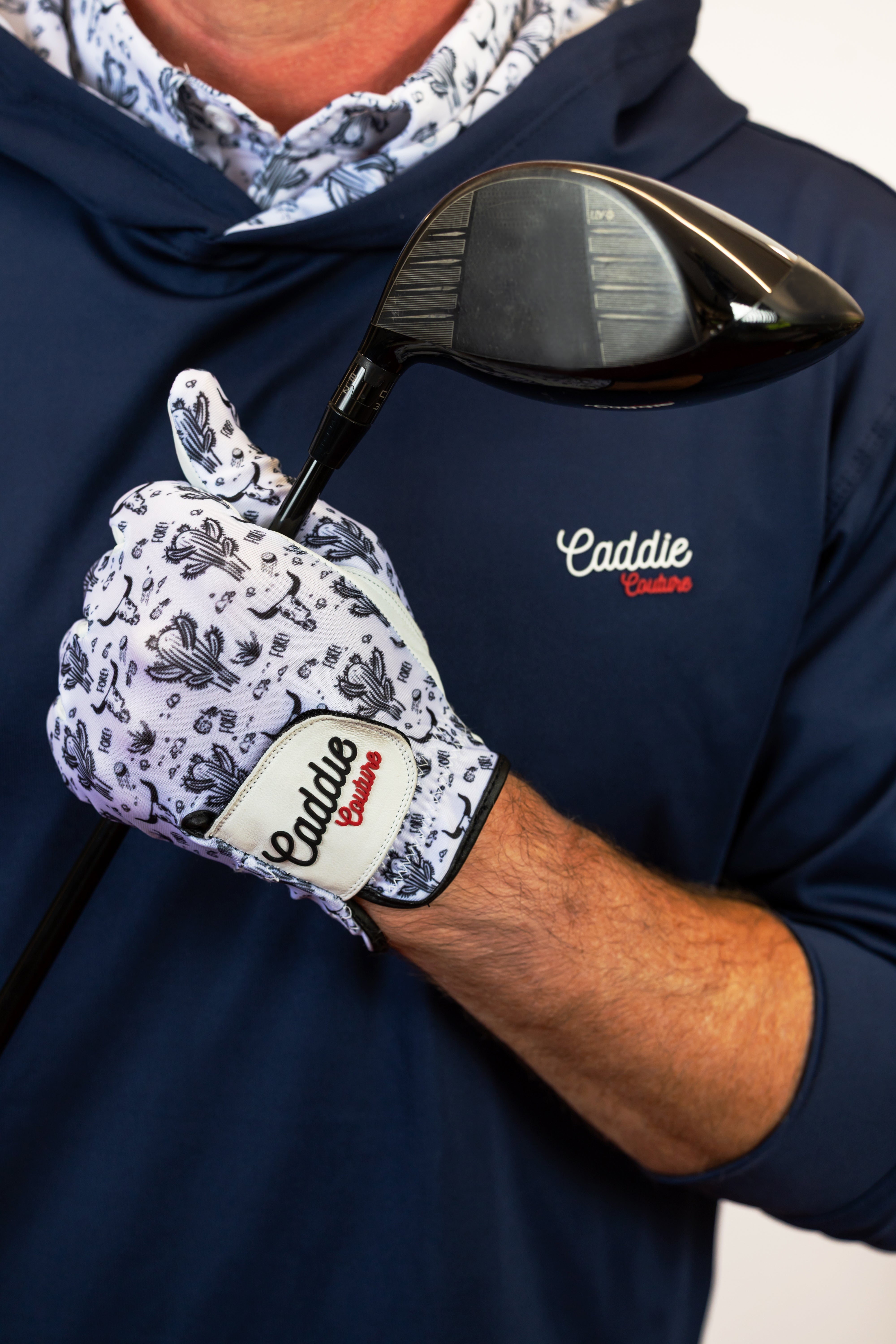 Person wearing a navy hoodie with 'Caddie' branding, holding a golf club with a matching glove.