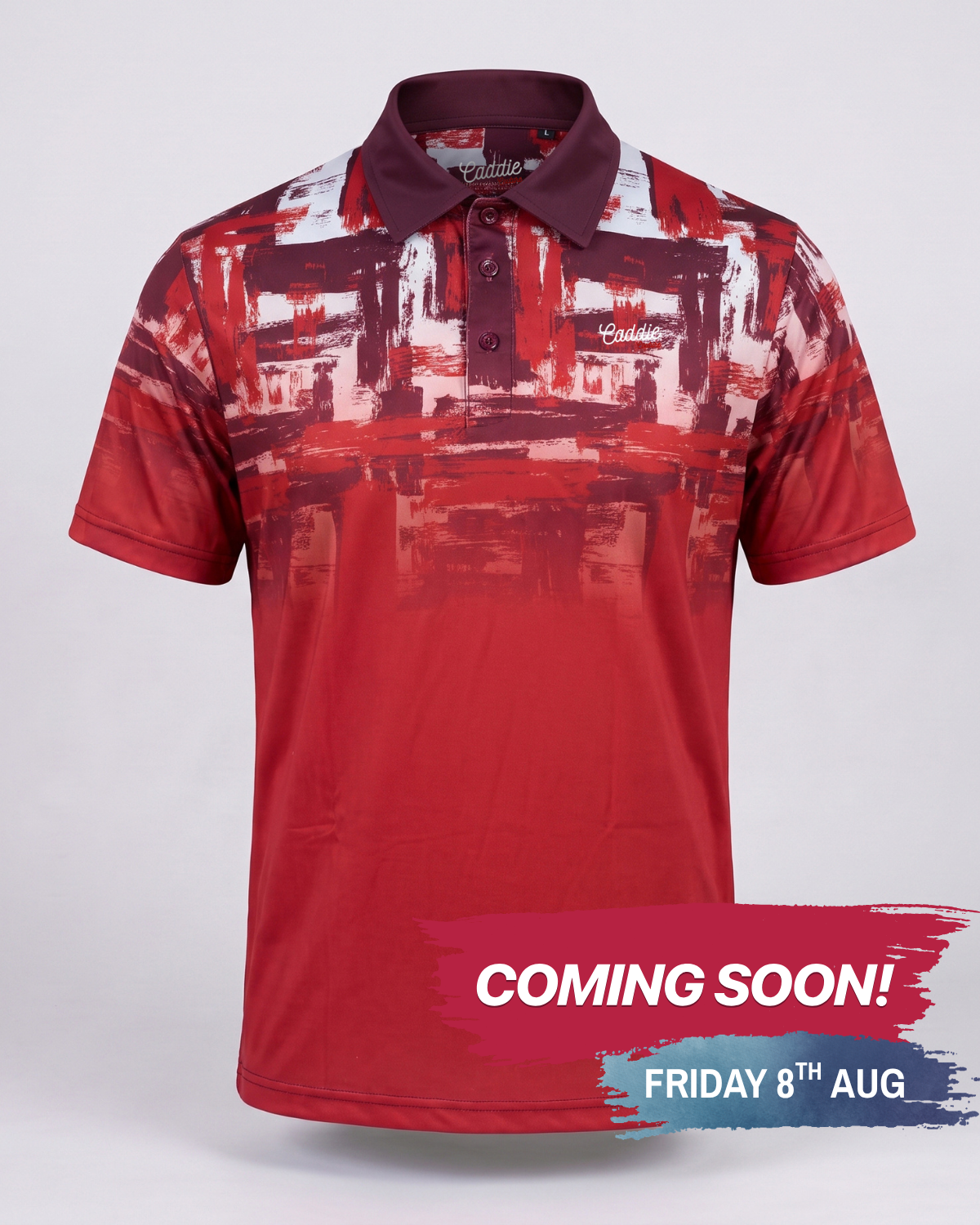A short-sleeve polo shirt with a red, white, and dark maroon abstract brushstroke pattern, shown on a light gray background with a 'COMING SOON!' promotional banner at the bottom.