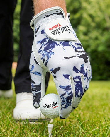 Golf glove with blue and white pattern holding a golf ball on grass