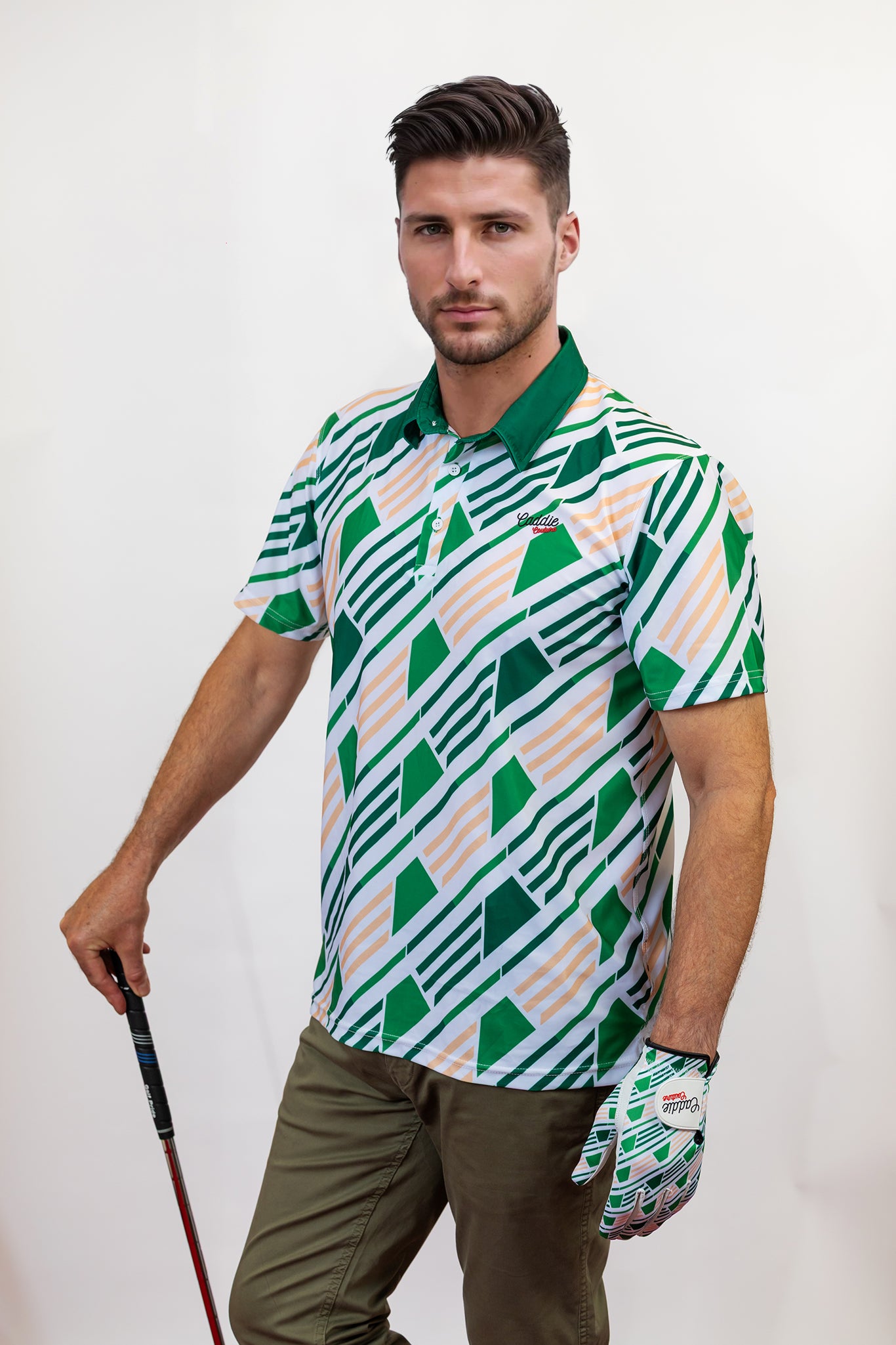 Man wearing a patterned golf shirt and holding a golf club on a plain background