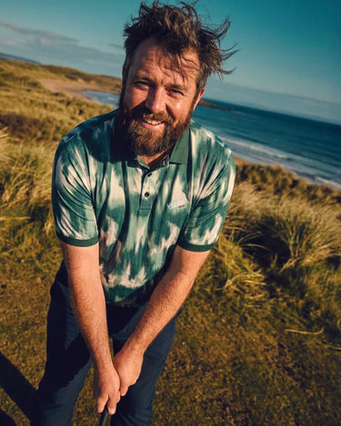 man holding golf club wearing green golf polo looking at camera