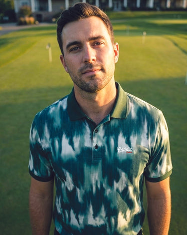 man looking straight at the camera on a golf course wearing green camo golf polo