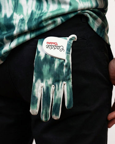 Tie-dye glove with brand logo hanging from a person's pocket against a neutral background