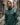 Man wearing a green jacket with a brand logo in an urban alleyway.