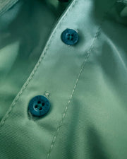 Close-up of a mint green satin-like shirt or blouse with two blue buttons on the front placket.