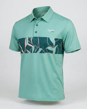 A short-sleeve polo shirt in mint green with a dark teal and pink tropical leaf pattern band across the chest, featuring a small 'Castille' logo on the left chest, displayed on a neutral light gray background.
