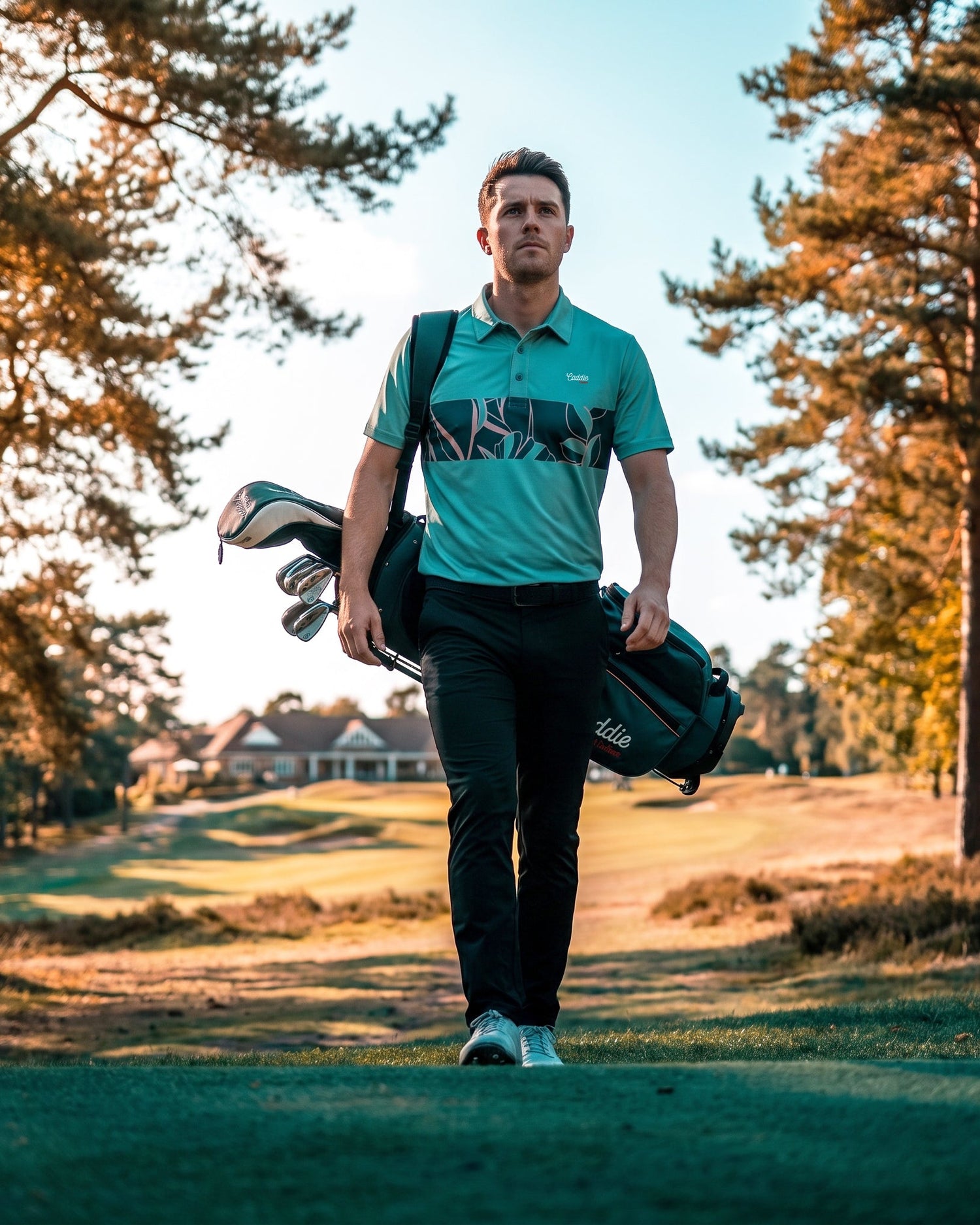 A man on a golf course wearing a teal and black polo shirt with a large 'NRA' logo, carrying a black golf bag over his shoulder.