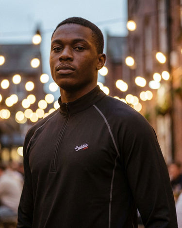 Man wearing a black jacket with a brand logo against a blurred background of lights