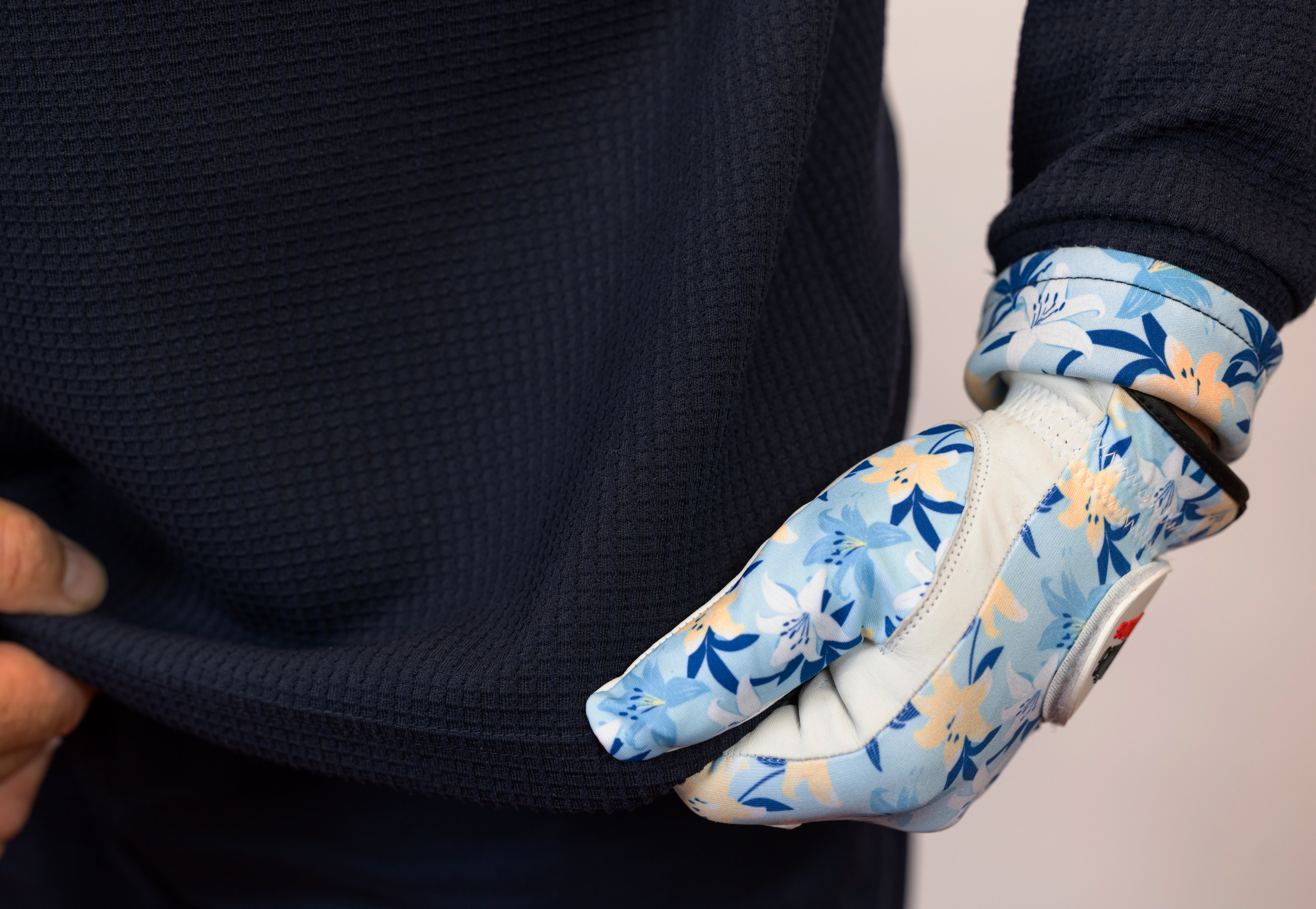 Person wearing a blue floral glove on a neutral background