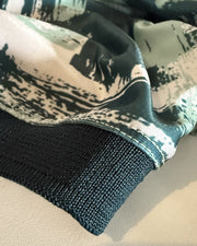 Close-up of a knit garment cuff with a dark teal ribbed edge and a matching printed fabric section above featuring a black, white, and muted green abstract brushstroke pattern.