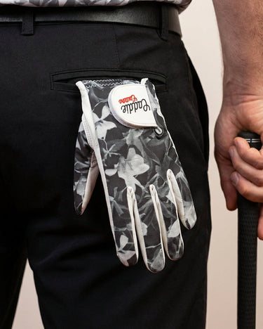 Person wearing a black floral-patterned golf glove on a plain background