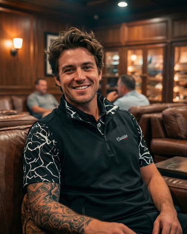 Man sitting on a leather couch in a bar or lounge setting, wearing a branded shirt.