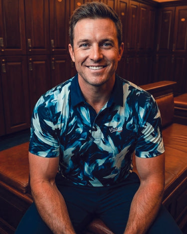 Man wearing a blue patterned shirt sitting in a wooden locker room.