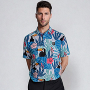 A man wearing a short-sleeved tropical print golf polo shirt with various colors, including blue, green, and pink, featuring a bird species, palm trees, and other foliage.