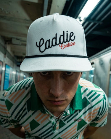 Person wearing a white cap with 'Caddie Couture' text in a subway setting