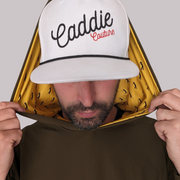 A person wearing a white golf hoodie with 'Caddie Couture' written on the cap in red. The hoodie has an olive green body with yellow golfer design details.
