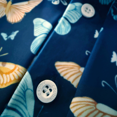 Close-up of a shirt with butterfly pattern and button, featuring the brand 'Caddie Couture"