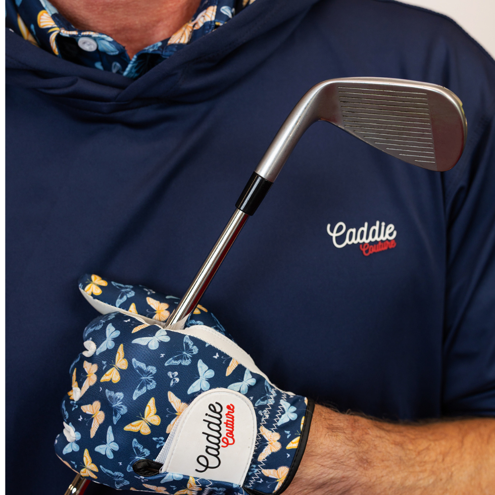Person wearing a navy hoodie with 'Caddie' logo, holding a golf club with a matching glove featuring butterfly pattern.