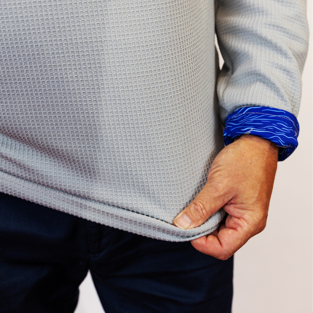 Person wearing a gray textured sweater with blue cuffs on a plain background